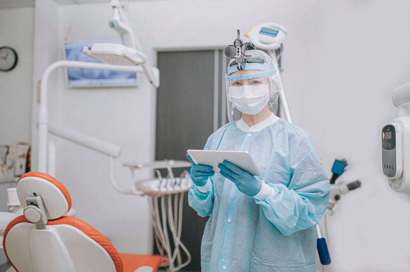 A dentist with PPE protective workwear for dental infection control holding digital tablet in dentist's office