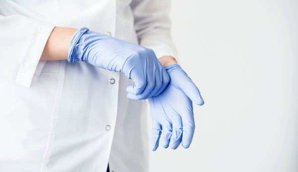 A dentist pulling on PPE gloves that are not counterfeit.